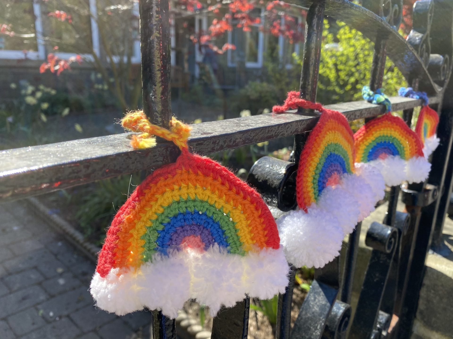 Row of bright coloured knitted rainbows hanging on a steel gate